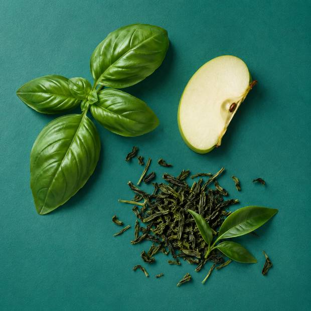Fresh basil, a green apple slice and loose green tea on teal.